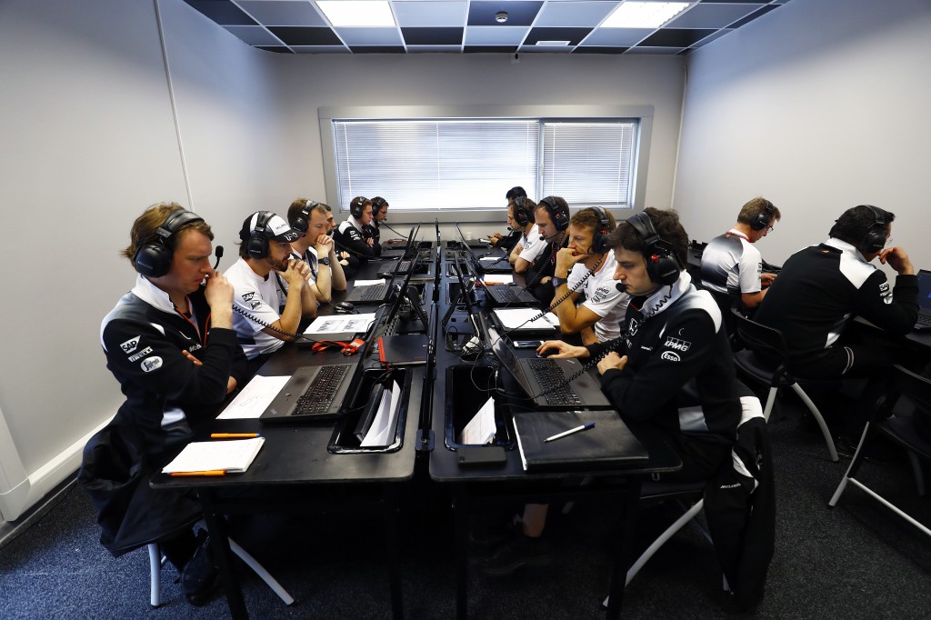 Jenson Button and Fernando Alonso study data with team members.